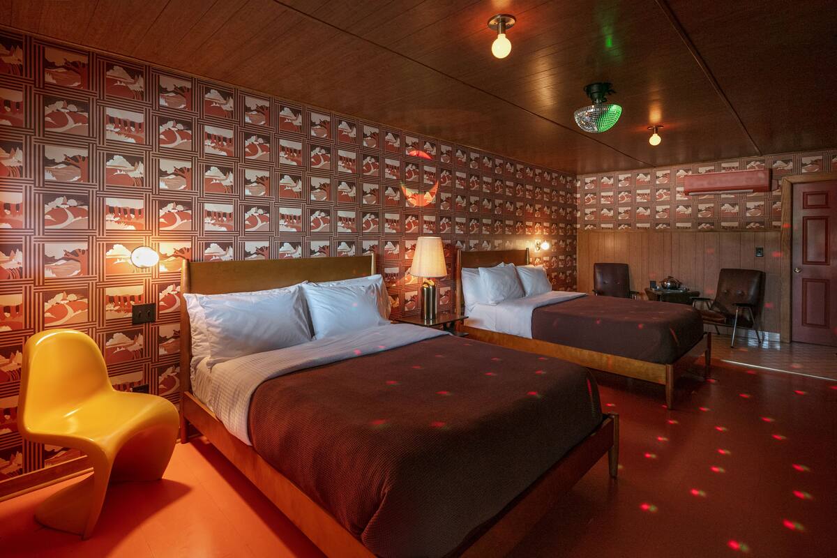 Habitación de hotel con dos camas, una silla y papel tapiz estampado.