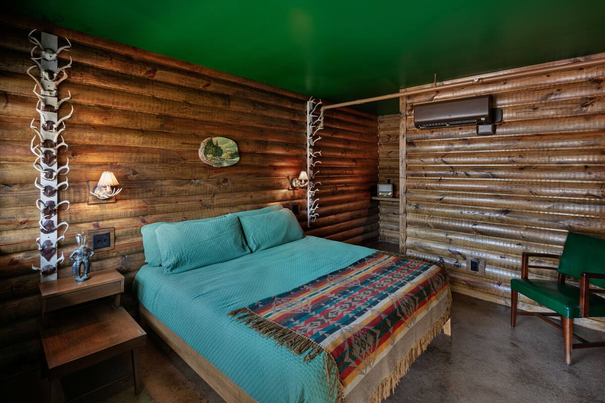 Una habitación tipo cabaña de madera con una cama, una silla, un calentador en la pared y un adorno mural.