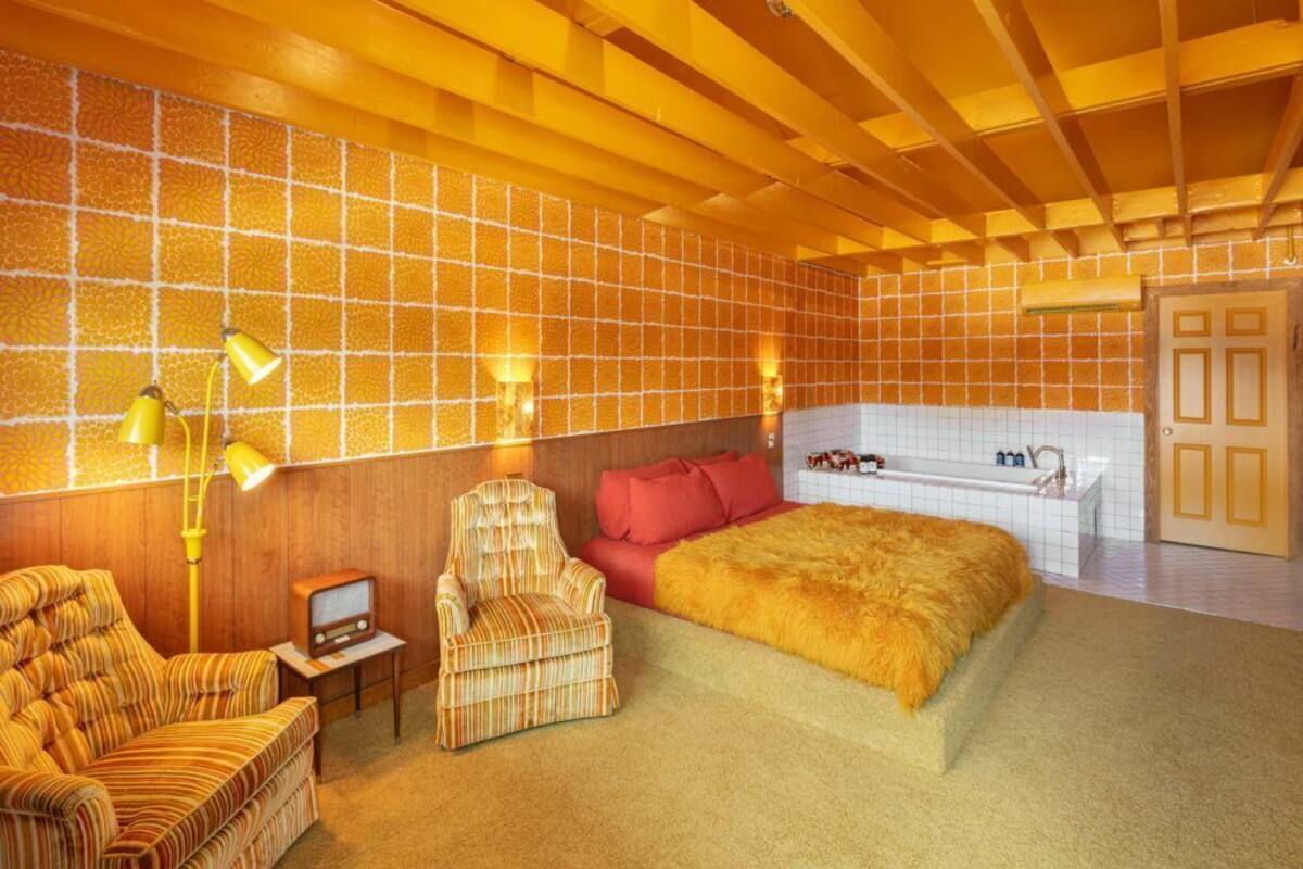 Habitación de hotel con una cama grande, un área de descanso con una silla y una mesita, una bañera y techo de madera.