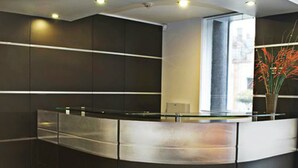 A modern reception desk with a curved design, a glass partition, and a large window providing natural light. - Flamante Hotel & Suite (Lima)