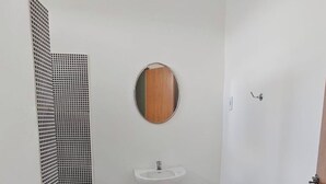 A small bathroom with a white sink, a round mirror, and a door. - Pousada Casa Bella (Itaberaba)