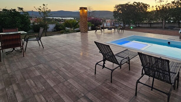 A wooden deck with a pool, outdoor furniture, and a stone pillar. - Pousada Casa Bella (Itaberaba)