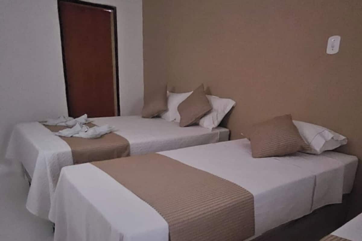 Quarto de hotel com três camas de solteiro, cada uma com colcha branca e manta marrom.
