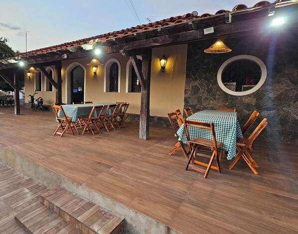Un patio al aire libre con mesas y sillas de madera, muros de piedra y puertas arqueadas.