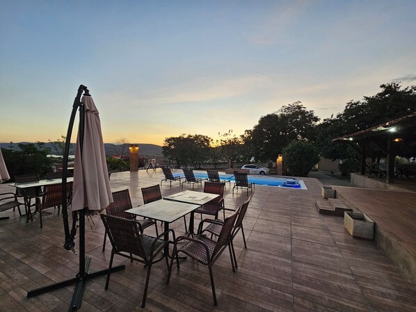 An outdoor patio with tables and chairs, a swimming pool, and a view of the landscape. - Pousada Casa Bella (Itaberaba)