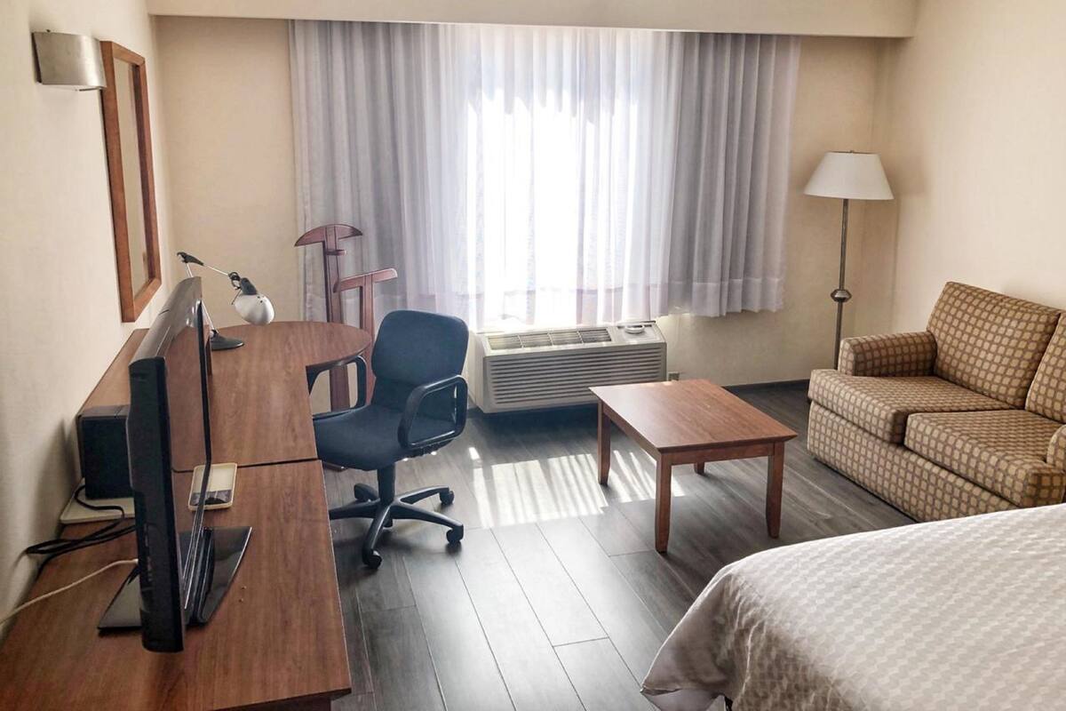 A hotel room with a desk, chair, bed, and a window with curtains.