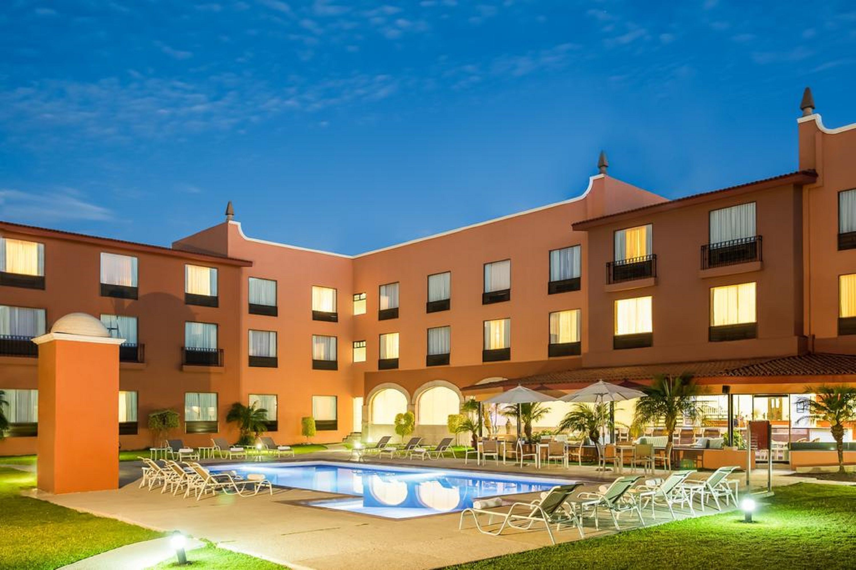 Un hotel con piscina, mobiliario de exterior y un patio.