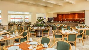 Un comedor amplio con varias mesas y sillas, un bufé central y un ventanal grande que proporciona luz natural.