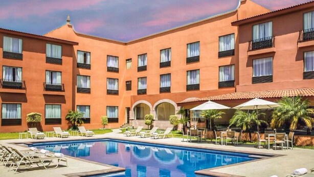 Un hotel con piscina, varios balcones y un patio con sillones y sombrillas.