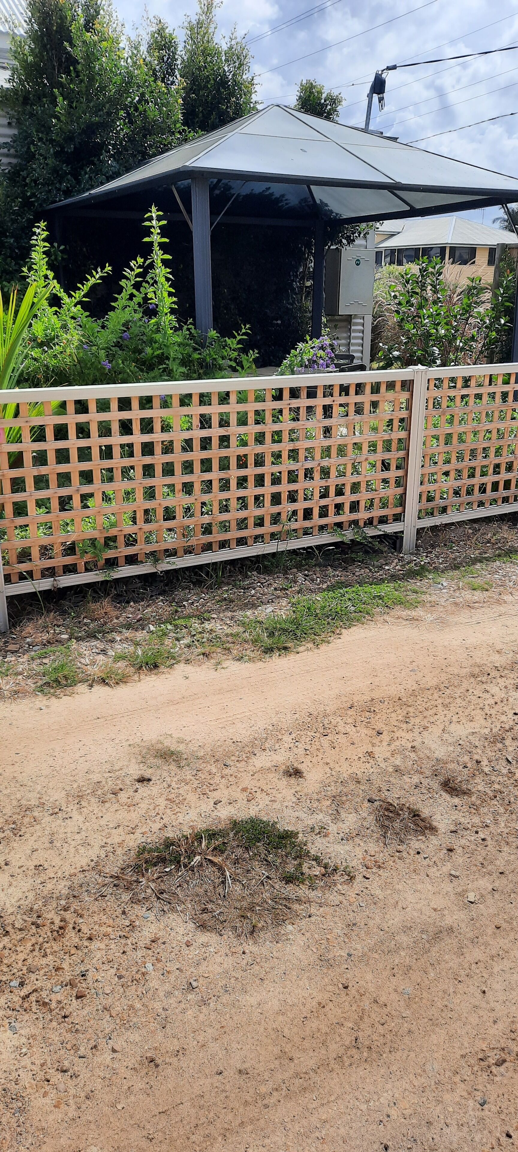 A fenced outdoor area with a dirt path, a metal structure, and greenery.