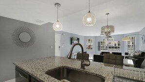 A modern kitchen with granite countertops, a stainless steel sink, and pendant lighting. - Completely Renovated 3/2 Close to Disney parks (Kissimmee)