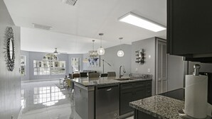 A modern kitchen with a central island, dark cabinetry, and a large window providing natural light. - Completely Renovated 3/2 Close to Disney parks (Kissimmee)
