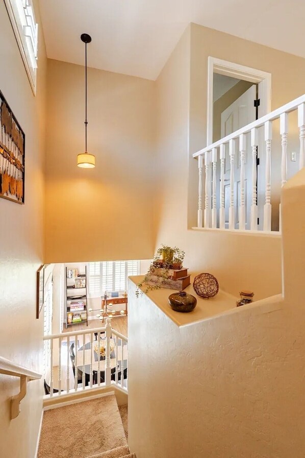 A staircase with a white railing, a hanging light fixture, and a small shelf with decorative items.
