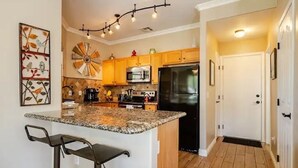 Una cocina con encimeras de granito, una isla central con taburetes de bar, armarios de madera, un refrigerador negro y un adorno mural.