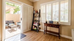 Una habitación con piso de madera, una estantería, un escritorio y una ventana con persianas.