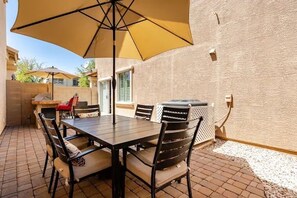 Un patio al aire libre con mesa y sillas, una sombrilla amarilla y una parrilla.