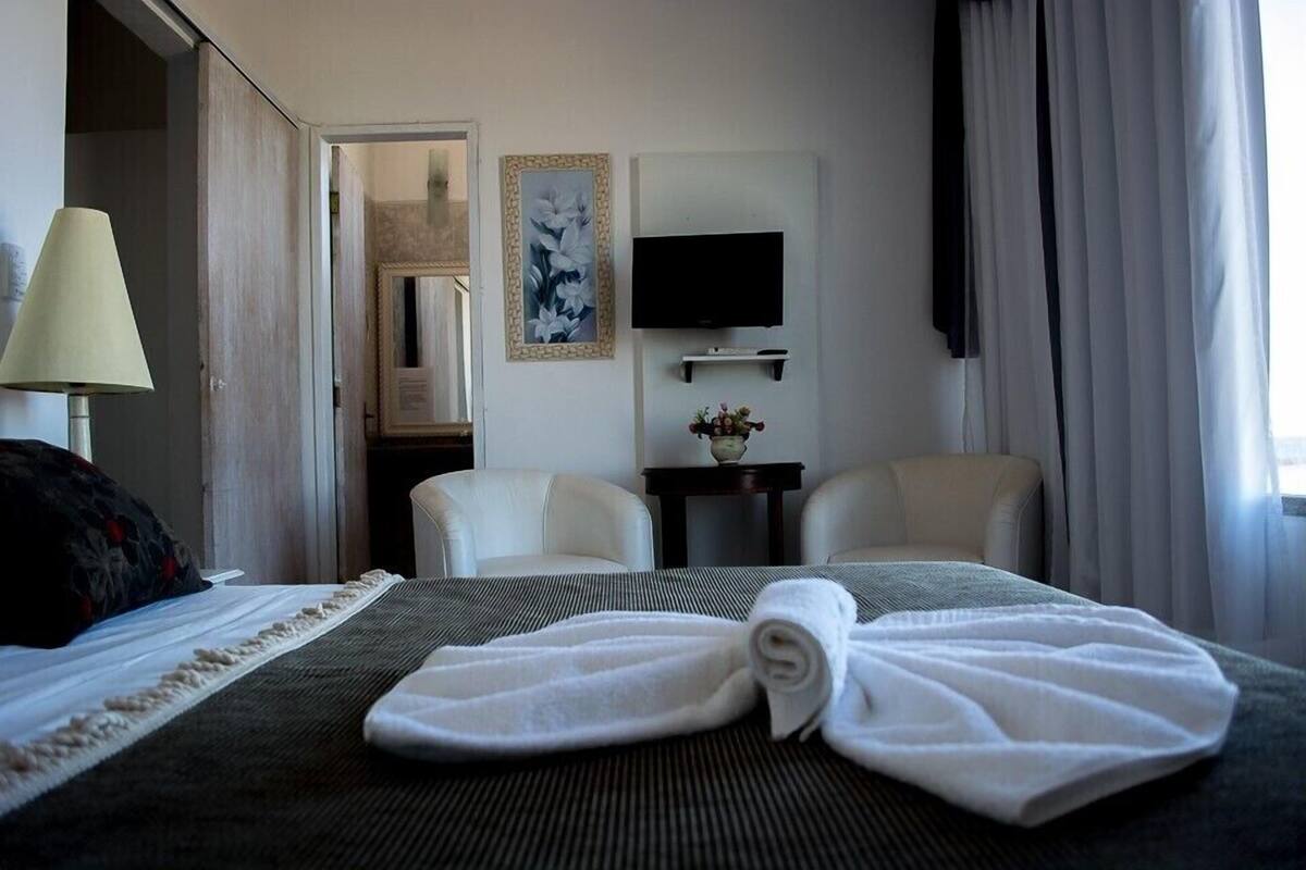 A hotel room with a bed, two chairs, a TV, and a painting on the wall.
