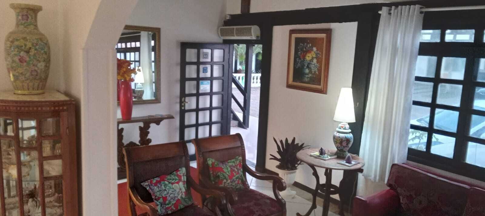 A room with a wooden chair, a small table with a lamp, a vase, and a painting on the wall.