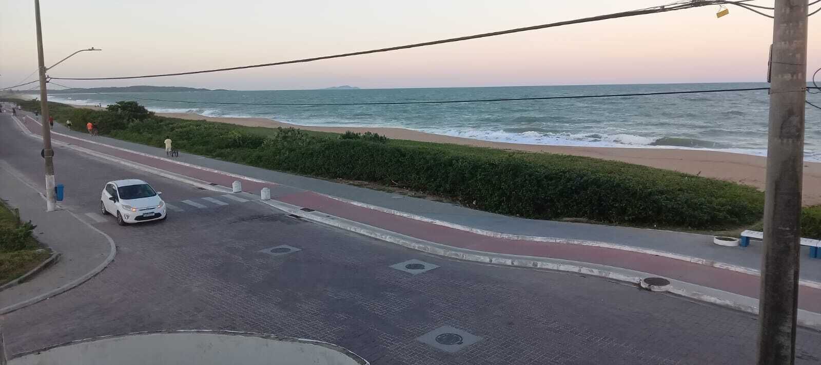 A coastal road with a white car parked on the side, a pedestrian path, and a view of the ocean.