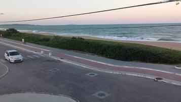 A coastal road with a white car parked on the side, a pedestrian path, and a view of the ocean.