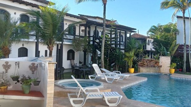 A pool area with lounge chairs, a hot tub, and a building with a white facade and black accents. - Atlantico Hotel (Rio das Ostras)