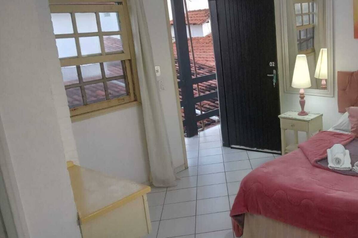 A bedroom with a bed, two bedside tables with lamps, a window, and a door leading outside.