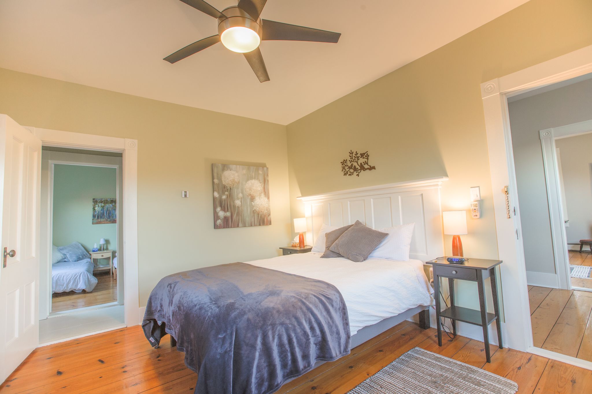 Une chambre à coucher avec un lit, des lampes de chevet, un ventilateur de plafond et un tableau au mur.