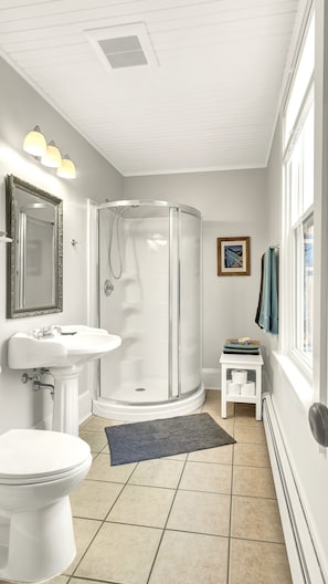 Ein Badezimmer mit Toilette, Waschbecken, Dusche und einem kleinen weißen Tisch mit Handtüchern.