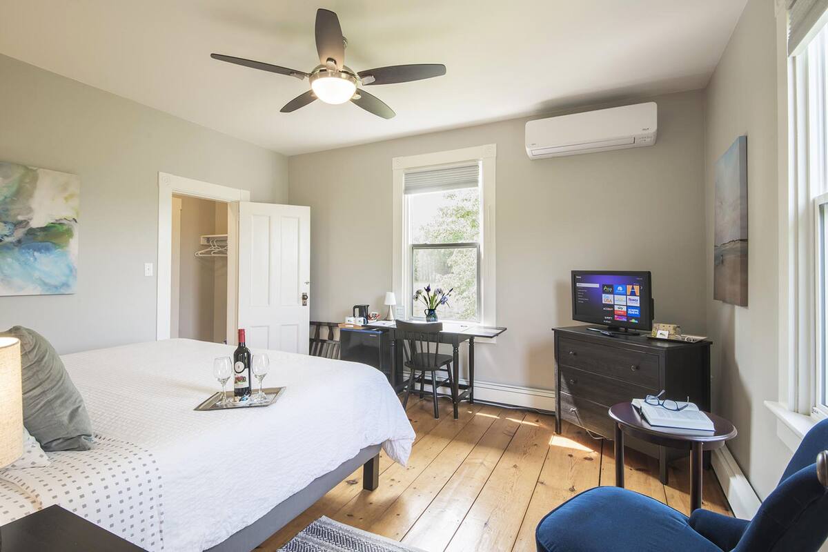 Un dormitorio con cama, escritorio, silla, televisión y ventana.