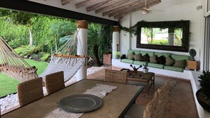 A covered patio with a table and chairs, a hammock, and a green sofa with cushions. - Stunnishing House in Cuernavaca with 20 people accommodation. (Los Limoneros)
