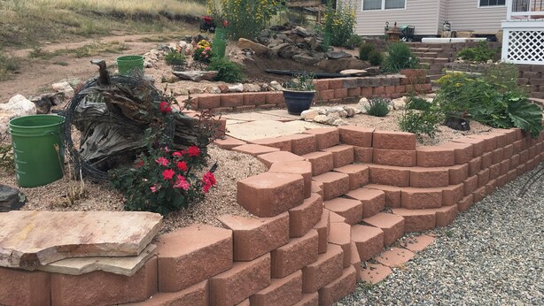 A landscaped garden with a brick retaining wall, potted plants, and a wooden log.