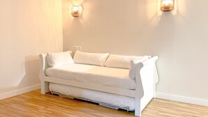 Een witte bank in een kamer met houten vloeren en twee wandlampen.
