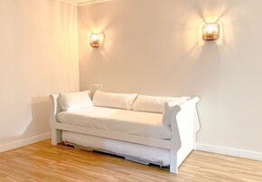 Un sofá blanco en una habitación con suelo de madera y dos lámparas fijadas a la pared.