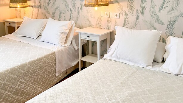 Een hotelkamer met twee bedden, een klein wit nachtkastje en een muur met een bladpatroon.