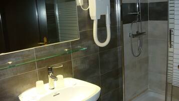 A bathroom with a white sink, a glass shelf, a handheld showerhead, and a mirror.