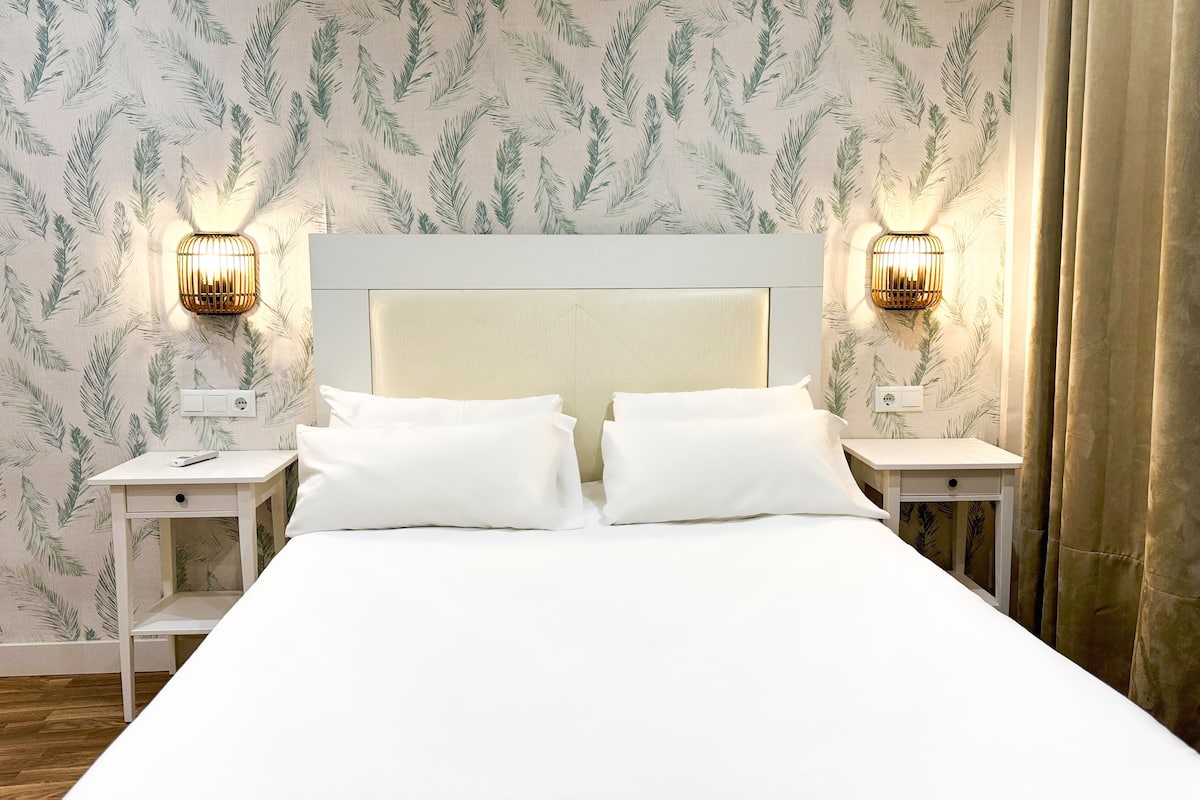 A neatly made bed with white linens, two bedside tables with lamps, and a patterned wallpaper.