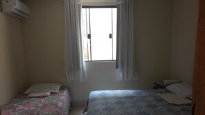 A bedroom with two beds, a window with curtains, and an air conditioning unit. - Hostel Le Monde (Angra dos Reis)
