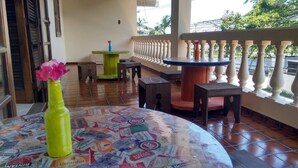 A room with a round table covered in beer bottle labels, a green vase with pink flowers, and a balcony with a white balustrade. - Hostel Le Monde (Angra dos Reis)