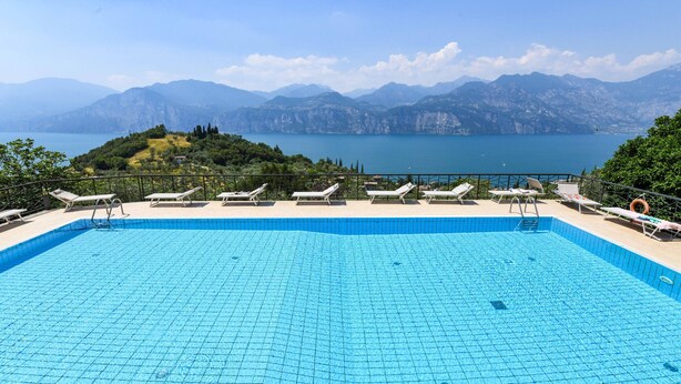 Piscina con sillas de descanso y vista a montañas y un lago.