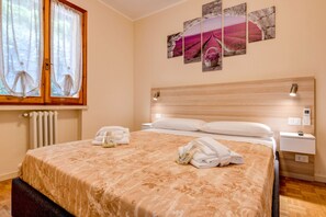 Una cama bien hecha con un edredón estampado con motivos florales, una mesita de noche con lámpara y una pared con tres cuadros enmarcados.
