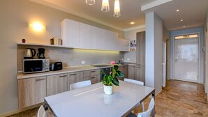 Cocina moderna con armarios blancos, encimera blanca, microondas, cafetera y una planta en maceta.