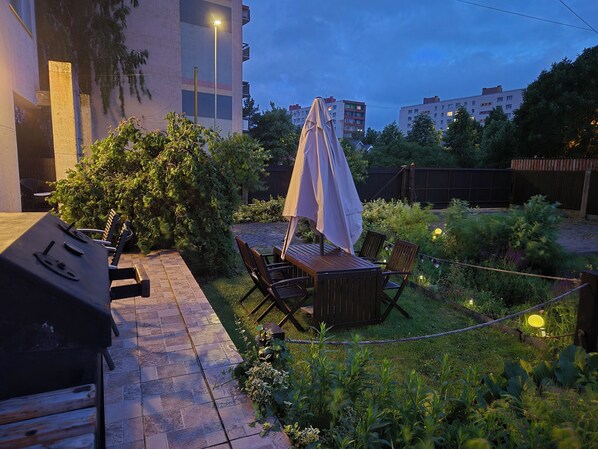 An outdoor patio with a grill, wooden table, chairs, and an umbrella.