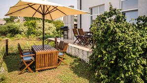 Una veranda esterna con tavolo e sedie di legno, un ombrellone grande e un barbecue.