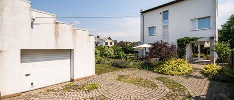 A residential area with a paved courtyard, a garage, and a modern two-story house with a small garden.