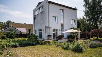 A modern two-story house with a patio area, a barbecue grill, and a variety of plants and shrubs in the garden.