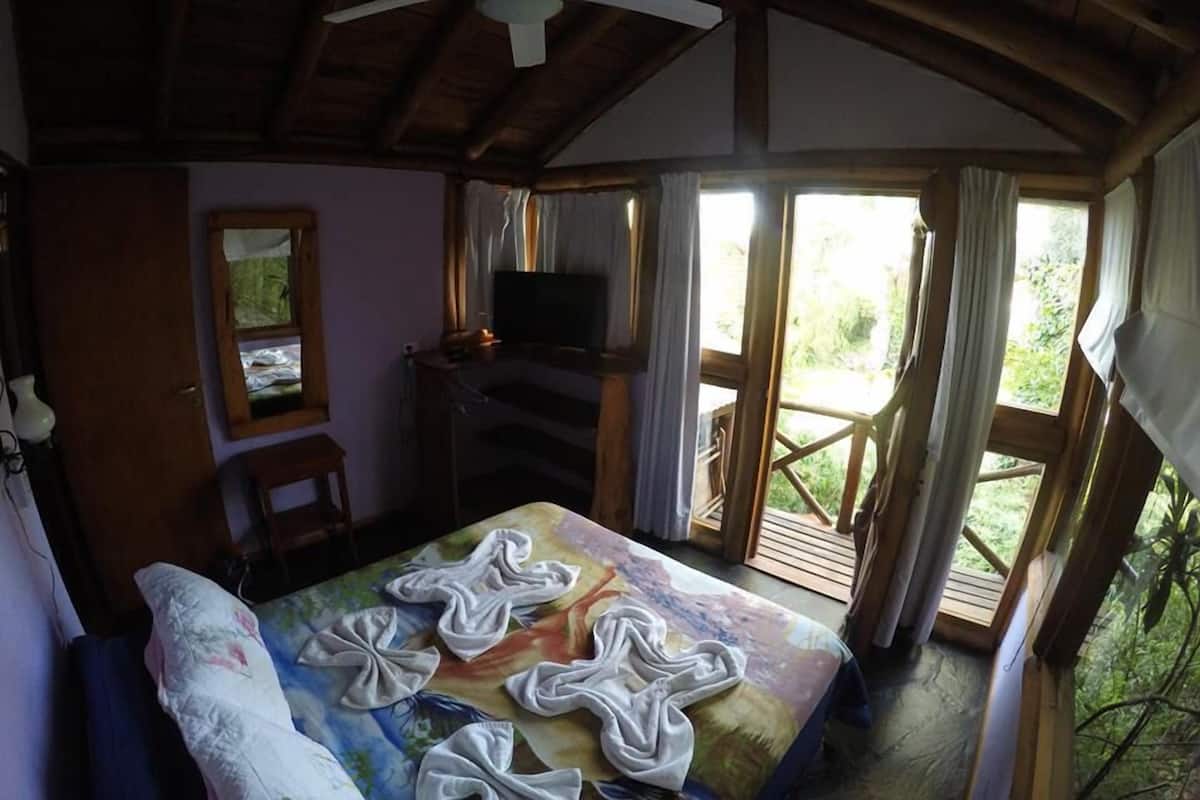 Una habitación con cama, ventilador de techo, televisión y ventana con cortinas.