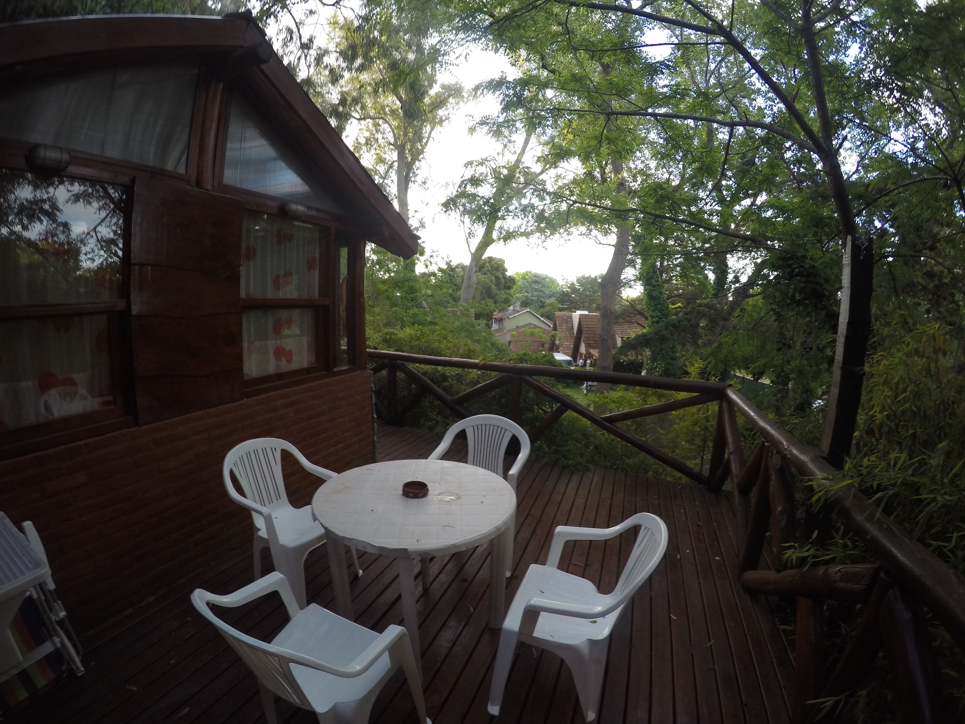Una terraza de madera con una mesa redonda y cuatro sillas de plástico blancas.