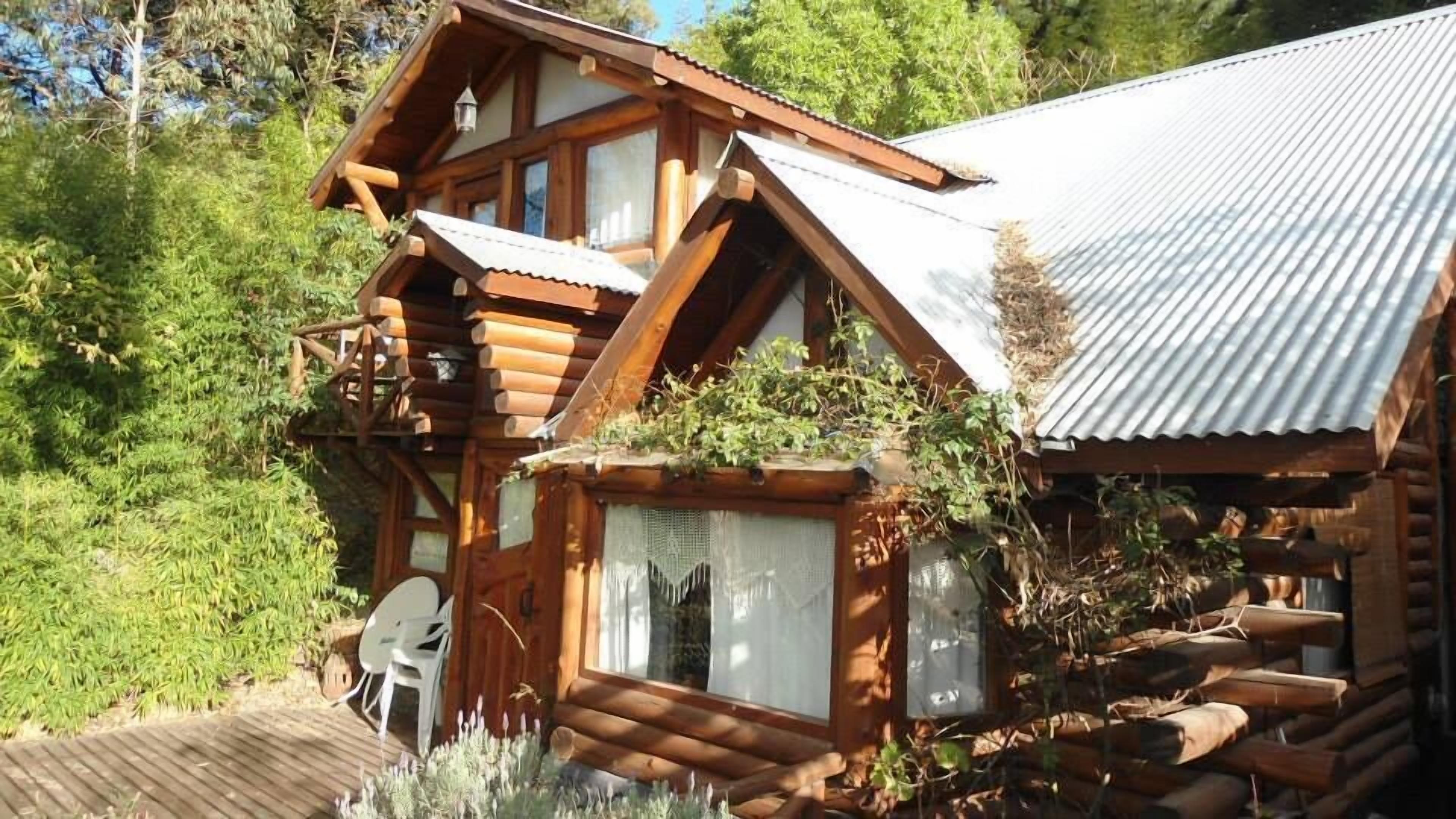 A log cabin with a balcony, a wooden deck, and a metal roof.