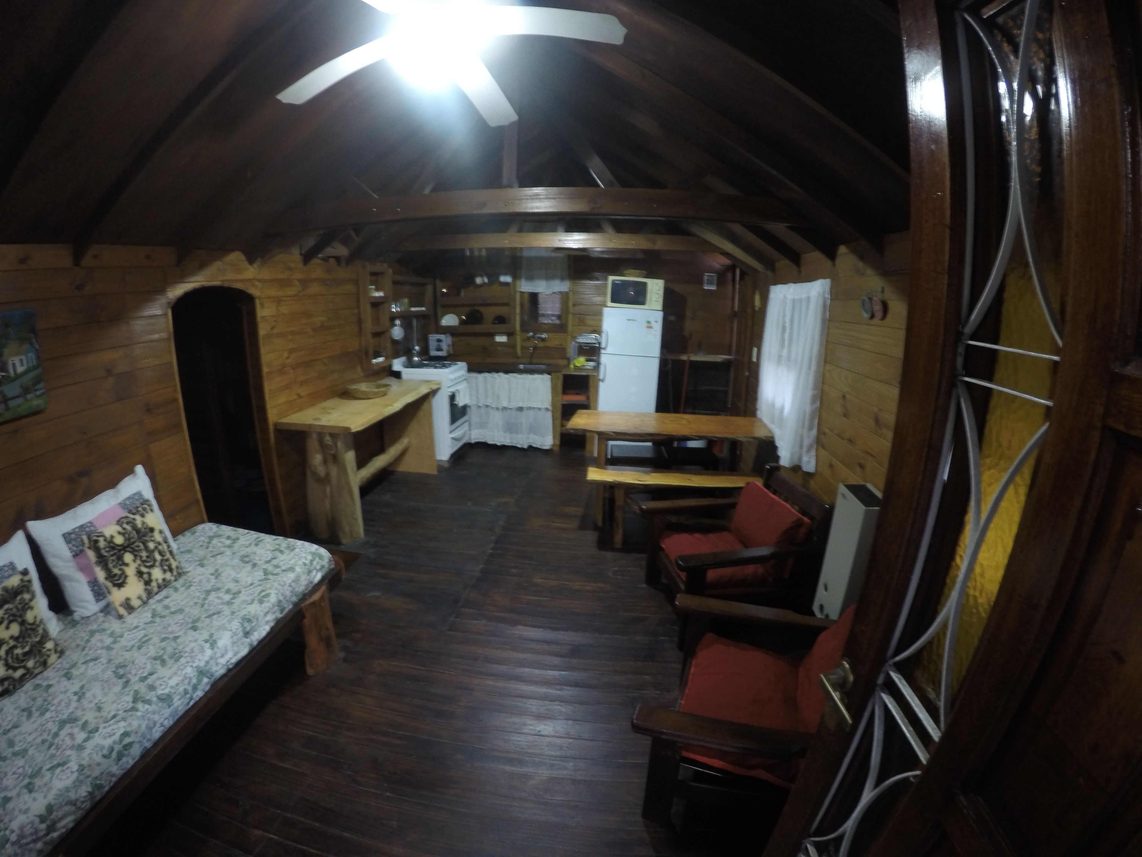 Interior acogedor de una cabaña con techo de madera, una mesa de comedor, un sofá y una zona de cocina.