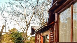 A wooden deck leading to a log cabin with stone accents and a view of trees. - Cabañas Manamar (Villa Gesell)